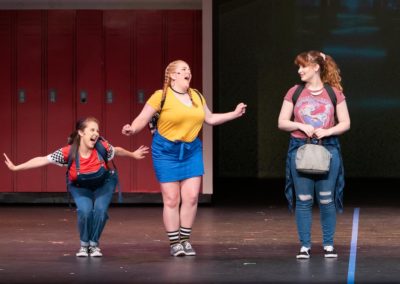 Scene from Freaky Friday: In a school hallway, HANNAH and GRETCHEN tell ELLIE that she "LOVES!" ADAM