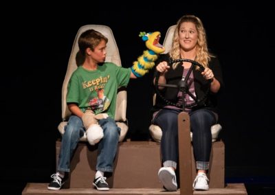 Scene from Freaky Friday: KATHERINE and FLETCHER are seated in a the car, FLETCHER talks as the puppet Angry Bob